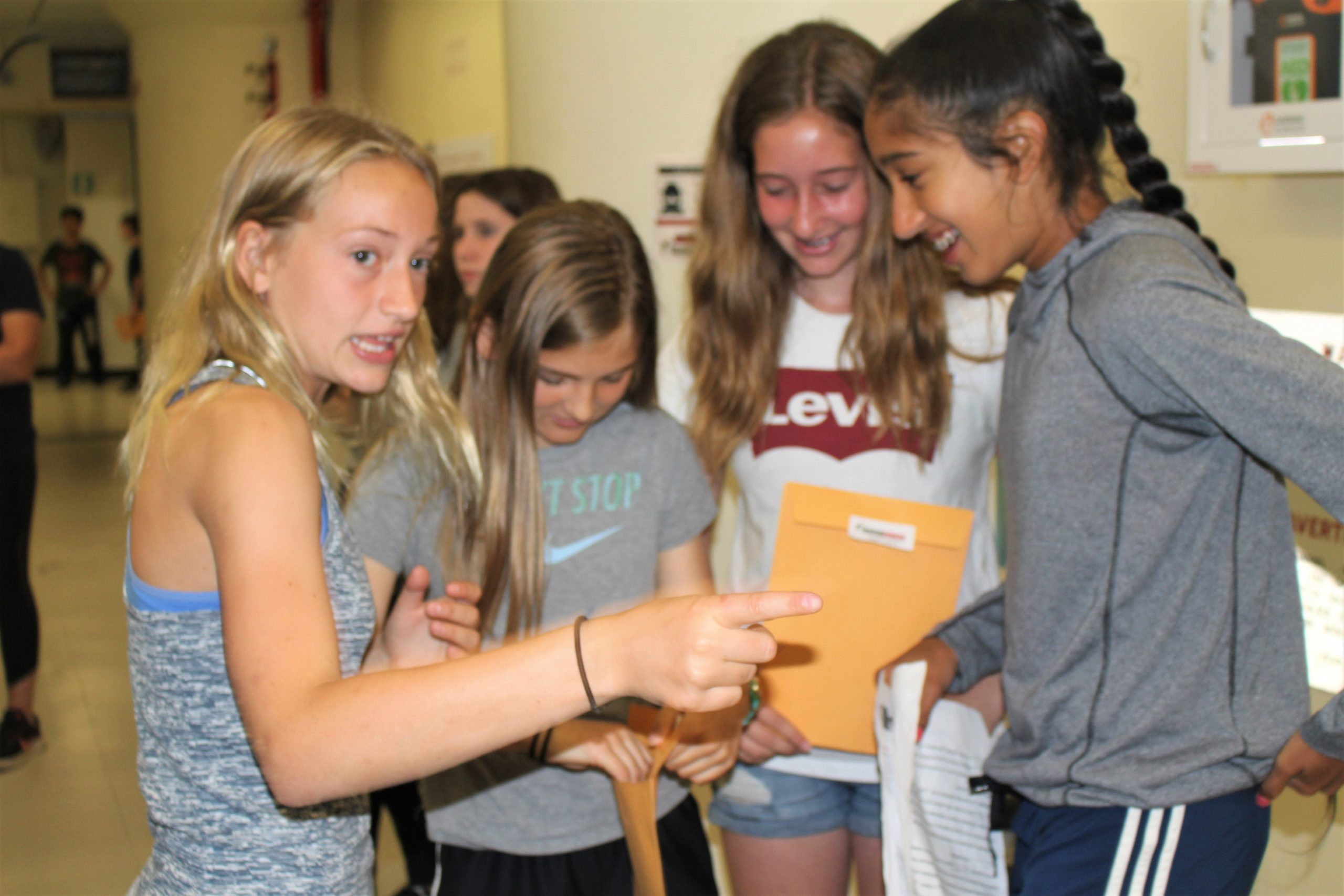 Four students look excitedly at clues in their hands, and one of them is pointing.