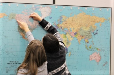 Two students stand to point out locations on a map of Canada.