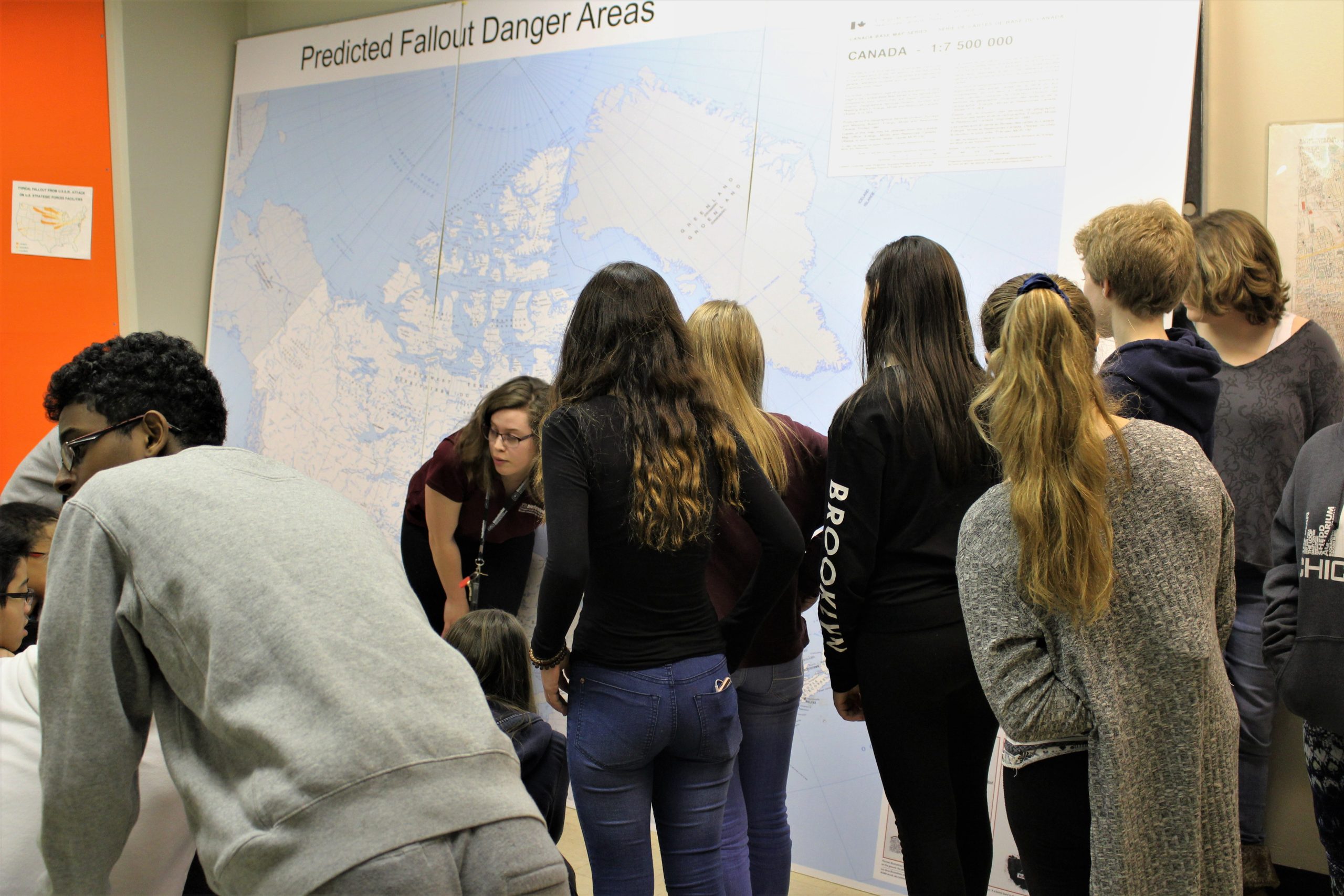A group of students are in discussion as they stand around a map of Canada showing fallout zones.