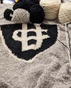 Work-in-progress knit sweater with Justin Case logo in the centre and six balls of yarn in the background for the 2022 AiR exhibition.