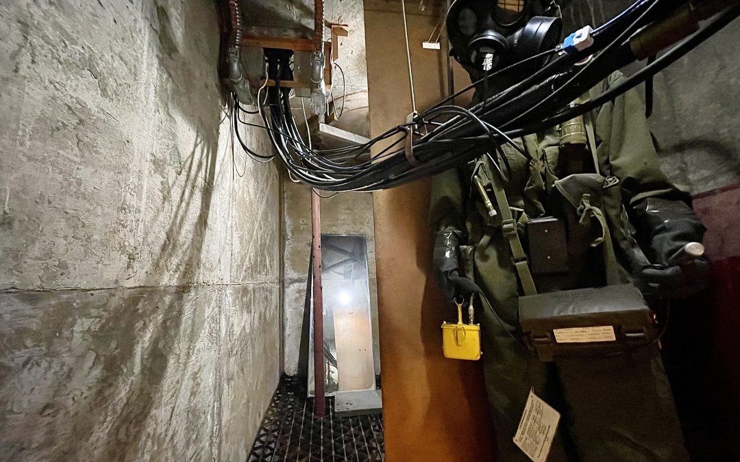 Mannequin dressed in Cold War apparel situated to the right in the Diefenbunker’s escape hatch. A large mass of wires drape in front of the mannequin and continue diagonally across the escape hatch and disappear into the top left corner.