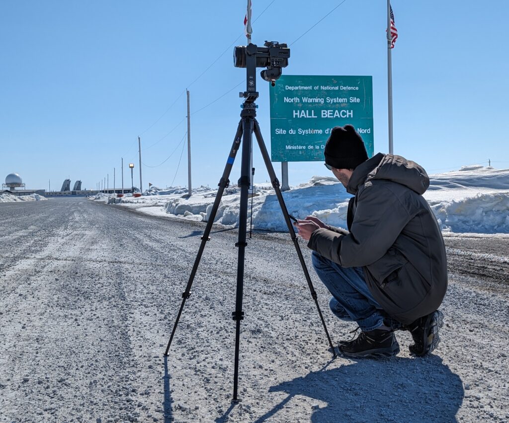 Camera equipment set up in front of the sign to the present-day North Warning System site Hall Beach, formerly the FOX-Main DEW Line site.