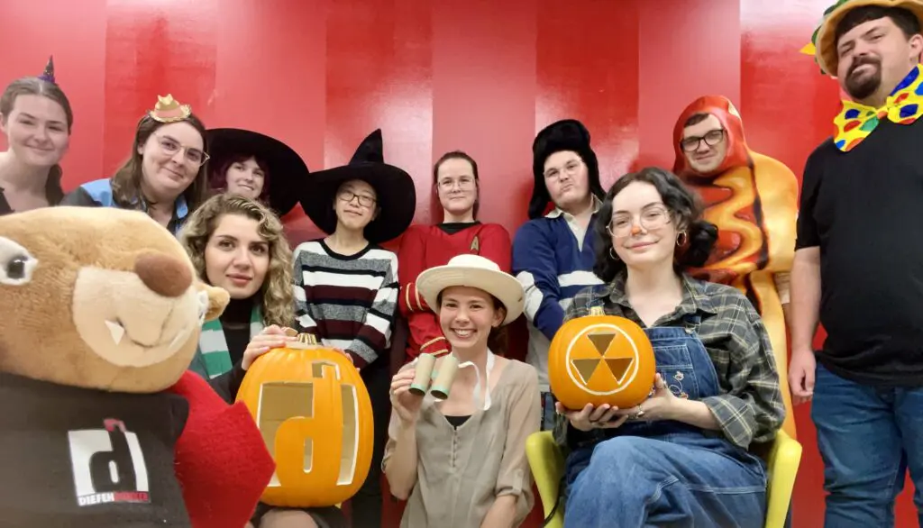 Group of people in Halloween costumes stand in front of a red wall.