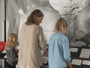 Two children and their parent stand in front of a museum display reading information.