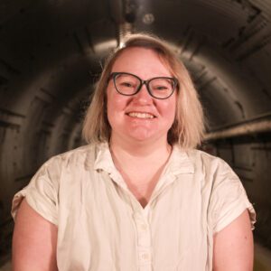 Smiling woman with glasses standing in a dimly lit tunnel.