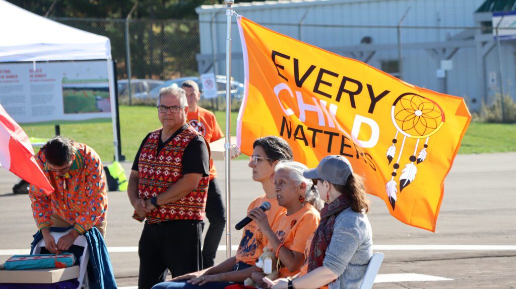 People gathered outdoors with a bright yellow banner reading 'Every Child Matters'.