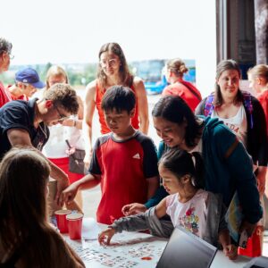 Group of kids wearing red look at merchandise on a table, with their parents standing behind them.