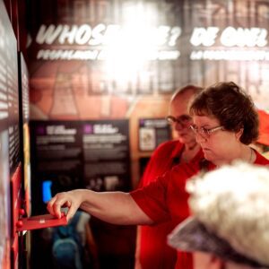A woman wearing red lifts up a text panel on the wall in a museum exhibition.
