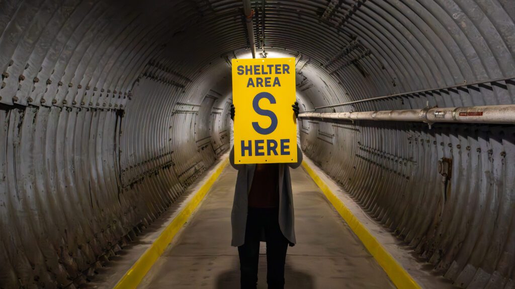 The Diefenbunker Museum Blast Tunnel, a member of staff is holding a sign. It reads: "SHELTER AREA S HERE"