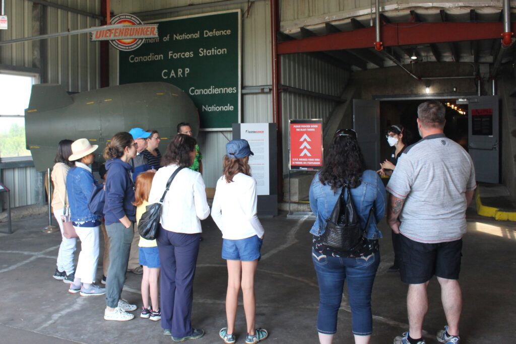 Families stand inside an industrial-style building, listening to a tour guide.