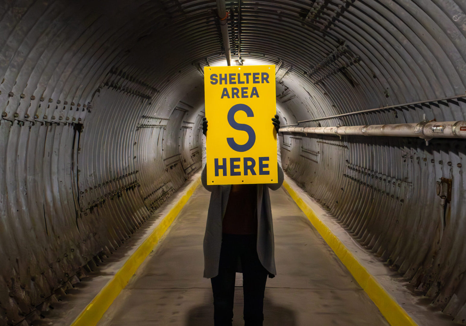 The Diefenbunker Museum Blast Tunnel, a member of staff is holding a sign. It reads: "SHELTER AREA S HERE"