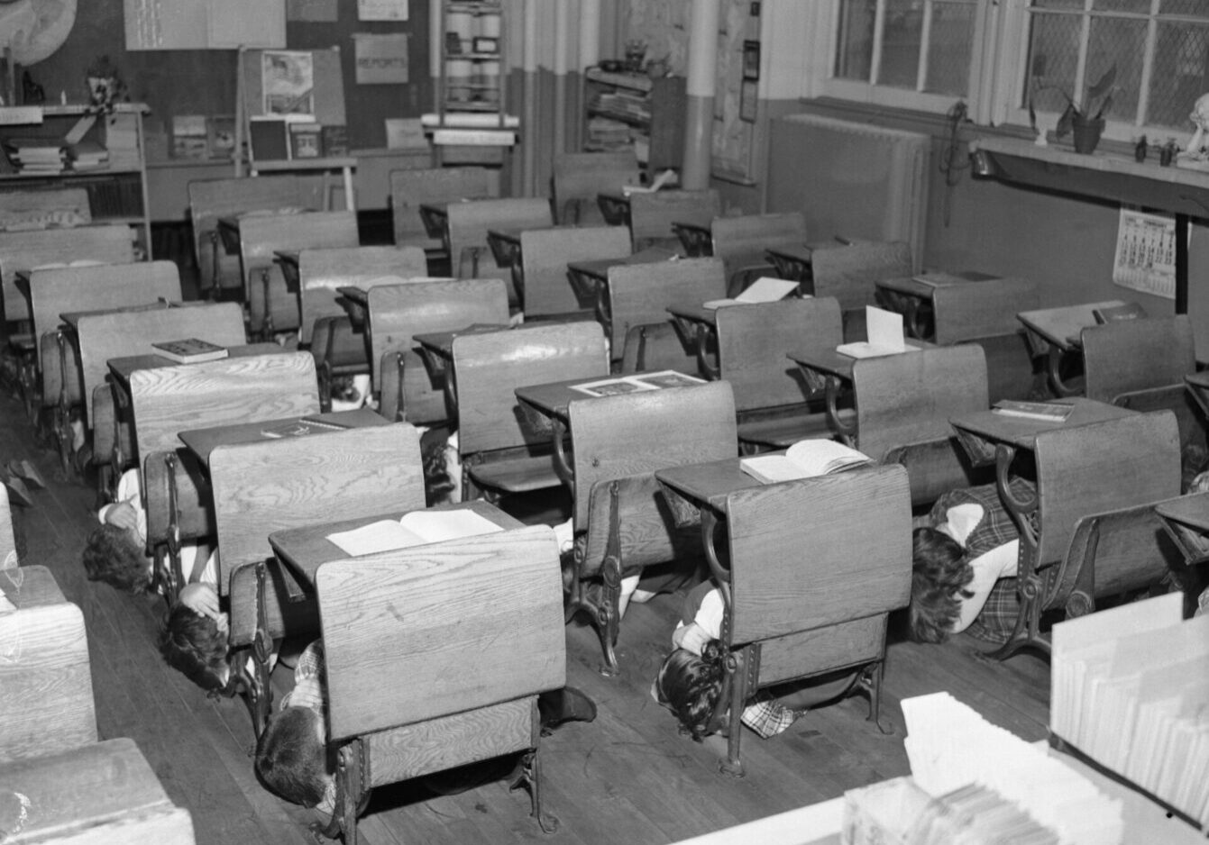 Over 15 students ducking and covering under their school desks.