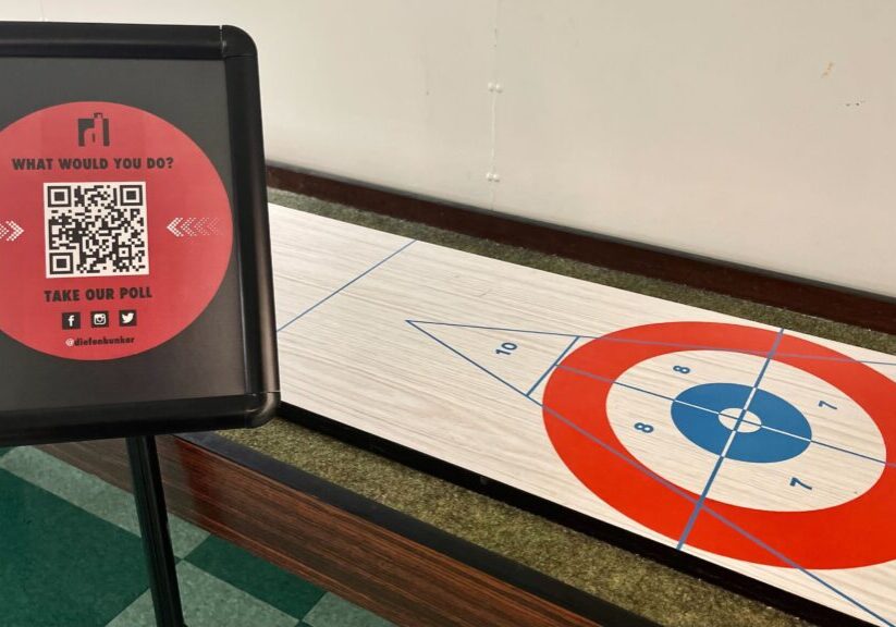 A tabletop shuffleboard game with a red puck near the scoring area.