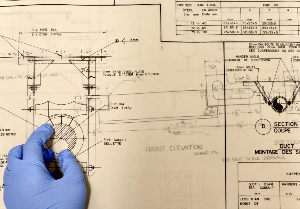 A person wearing gloves and writing on a blueprint.